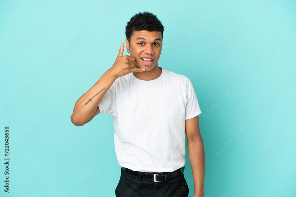 Young African American man isolated on blue background making phone gesture. Call me back sign Young African American man isolated on blue background making phone gesture. Call me back sign