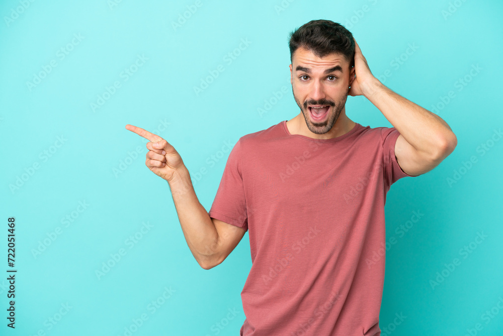 Young caucasian man isolated on blue background surprised and pointing finger to the side Young caucasian man isolated on blue background surprised and pointing finger to the side