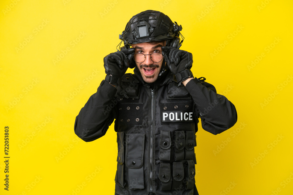 SWAT caucasian man isolated on yellow background with glasses and surprised SWAT caucasian man isolated on yellow background with glasses and surprised