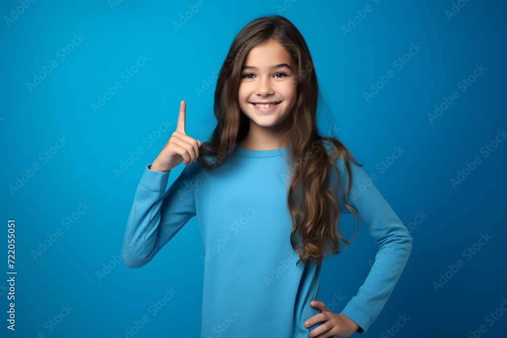 Full-Size Photograph of a Positive and Gorgeous Girl, Indicating with her Finger towards an Empty Space. Exuding Positivity and Charm, Isolated Against a Striking blue Background. Full-Size Photograph of a Positive and Gorgeous Girl, Indicating with her Finger towards an Empty Space. Exuding Positivity and Charm, Isolated Against a Striking blue Background.
