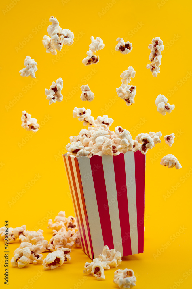 Popcorn in red and white striped paper box isolated on yellow background Popcorn in red and white striped paper box isolated on yellow background