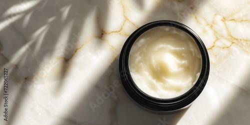 Wide banner displaying an open jar of moisturizer on a marbled surface with natural light casting shadows with copy space for make up industry and beauty salons  photo
