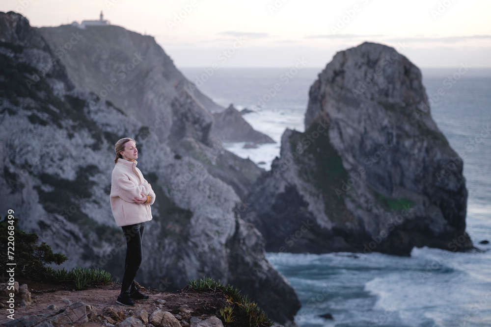 A woman looks at the ocean while standing on rocks, Atlantic coast, Sintra, Portugal.