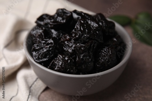 Sweet dried prunes in bowl on brown table, closeup