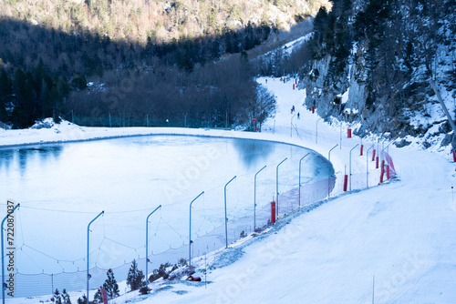 skiers pass by a frozen lake on a ski slope in the french pyrenees. ski resort of Arette