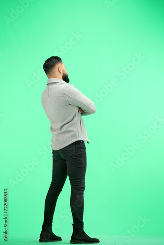 A man, full-length, on a green background, crossed his arms