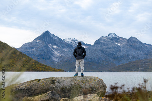Persona contemplando montañas rocosas con nieve desde una roca a orillas de un fiordo photo