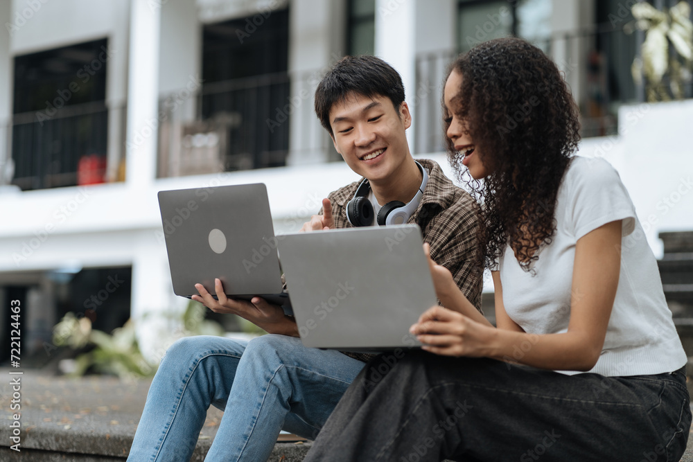 Diversity, college student focusing on laptop work or reading while other classmates in the background, outdoor portrait on campus campus. Diversity, college student focusing on laptop work or reading while other classmates in the background, outdoor portrait on campus campus.