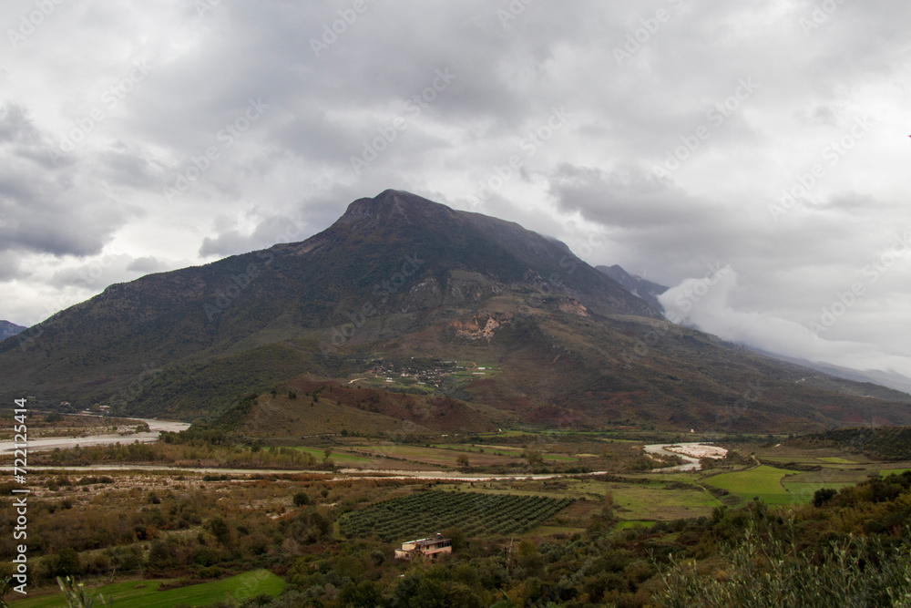 the mountain in Albania on a cloudy day, river near the mountain, house and vineyard against the backdrop of the mountain, albania in november the mountain in Albania on a cloudy day, river near the mountain, house and vineyard against the backdrop of the mountain, albania in november