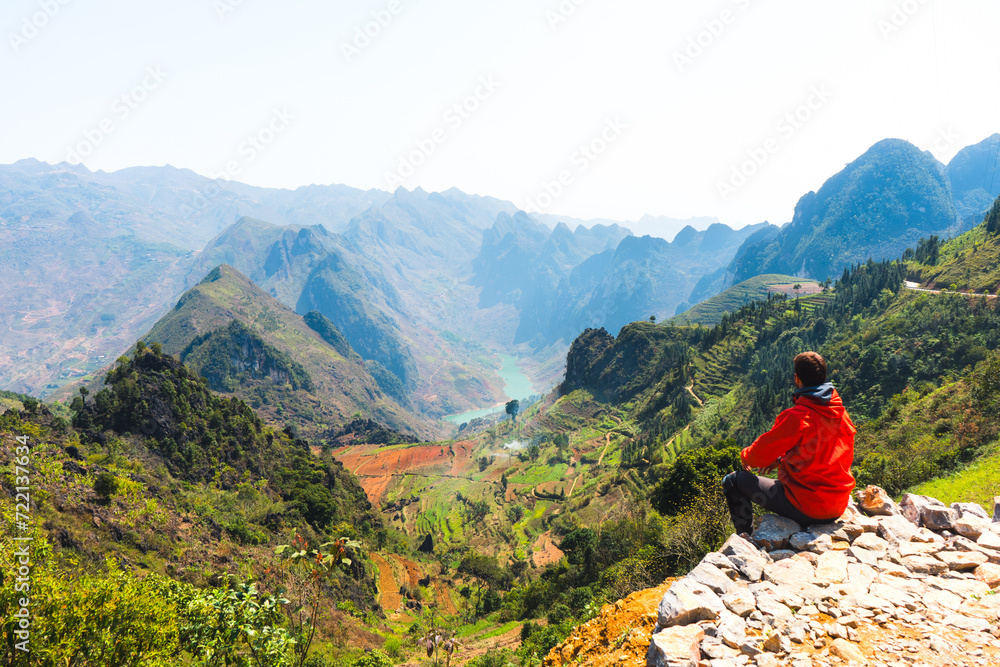 A person in an orange jacket sitting and overlooking a scenic mountain valley