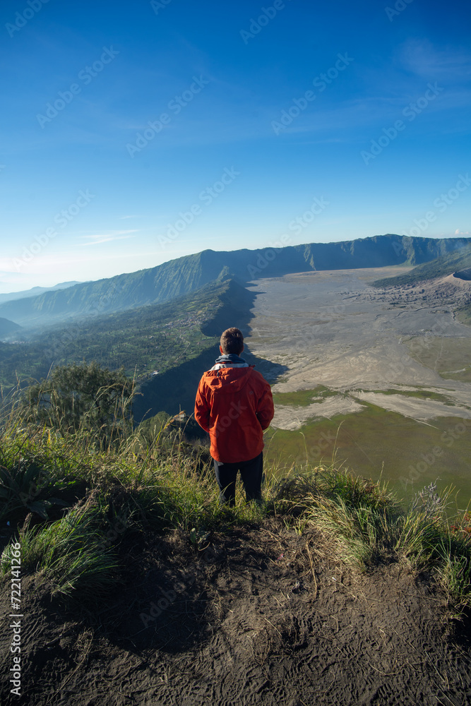 A person in a red jacket admiring the vast expanse of a mountainous landscape.