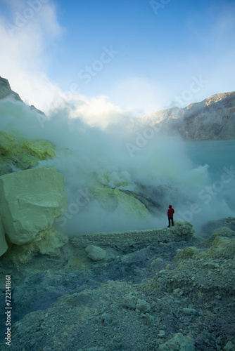 A lone explorer stands near a steaming vent at a sulfur-rich volcanic site.