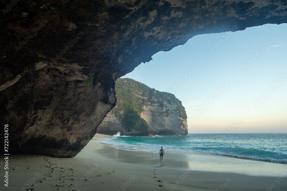 A person walking on a serene beach viewed from a cave opening
