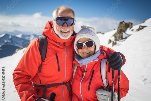 Happy senior couple in winterwear standing on top of a snowy mountain