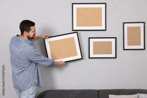 Man hanging picture frame on gray wall indoors