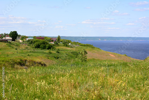 grassy hill with cottages on the top and blue river coy space 