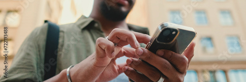 Close-up of young man with beard dressed in an olive color shirt uses phone map app on the old city background, Panorama