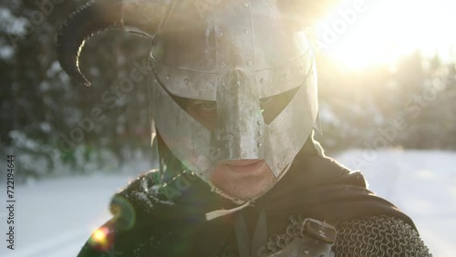 Medieval fantasy warrior in a horned helmet, posing against the backdrop of sunset in a winter forest. Rays of the sun, glare. Camera movement, selective focus. photo