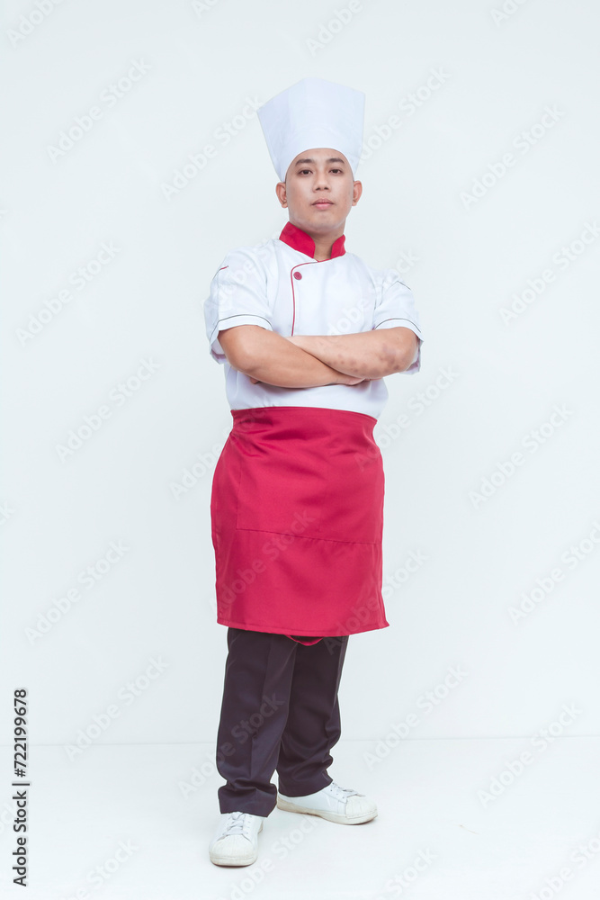 A short Asian chef in traditional uniform and hat standing with arms crossed on a white background, portraying professionalism. Full body photo. A short Asian chef in traditional uniform and hat standing with arms crossed on a white background, portraying professionalism. Full body photo.