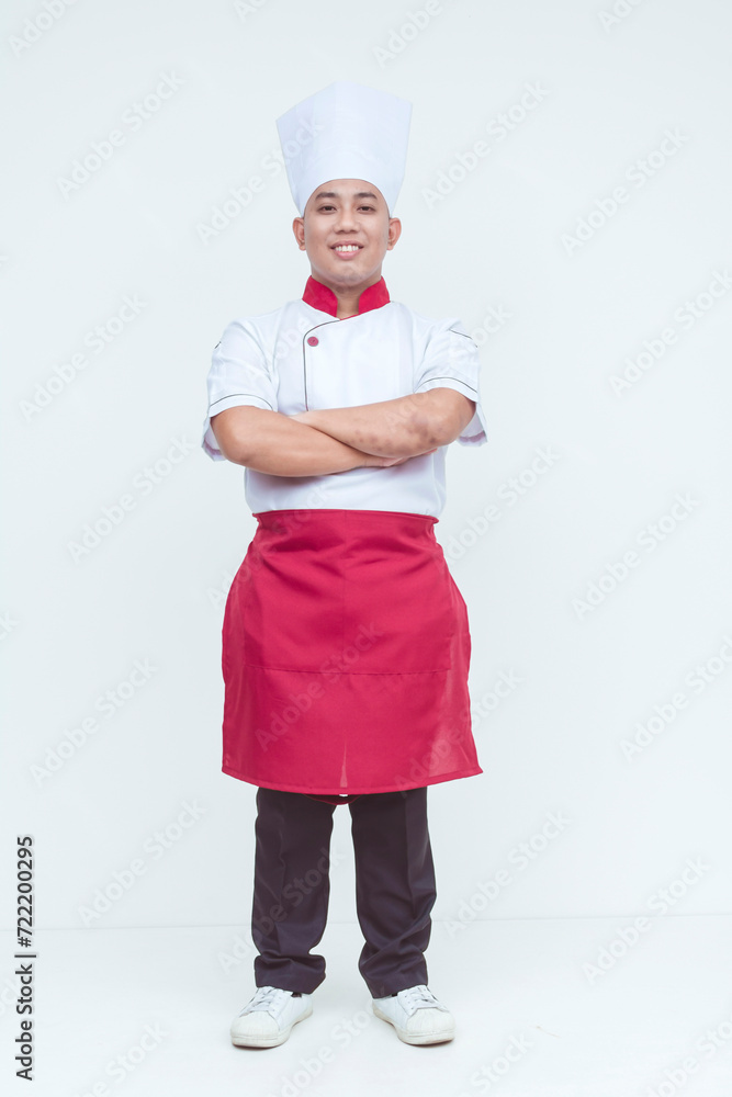 Portrait of a smiling Asian chef wearing a traditional white hat and red apron, confident stance isolated on a white background. Portrait of a smiling Asian chef wearing a traditional white hat and red apron, confident stance isolated on a white background.