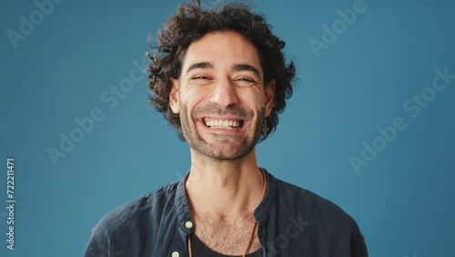 Close up, laughing man looks at camera isolated on blue background in studio photo