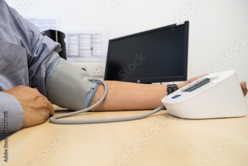 Close up of Asian man in 50s checking blood pressure with instrument in the work office