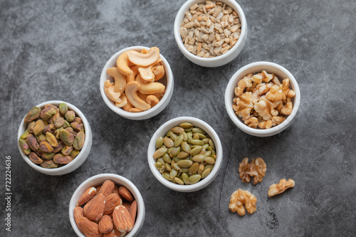 Pistachios, almonds, cashews, pumpkin seeds, sunflower seeds, and walnuts on a gray counter top.