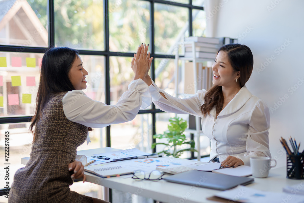 Two young Asian businesswoman smiling happy giving high five at the office. Young Asian woman or intern who successfully completes her goals. Two young Asian businesswoman smiling happy giving high five at the office. Young Asian woman or intern who successfully completes her goals.