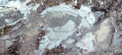 Texture of a frozen puddle with mud and slush, and the surface of the icy water. Winter outside ground in the countryside