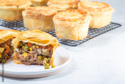 Sliced beef pot pie on plate, pies on cooling rack, horizontal, copy space