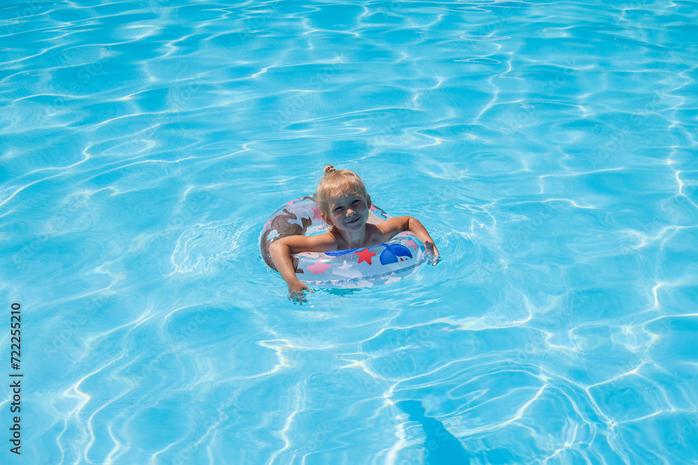 Smiling baby girl swims with an inflatable ring in a summer pool