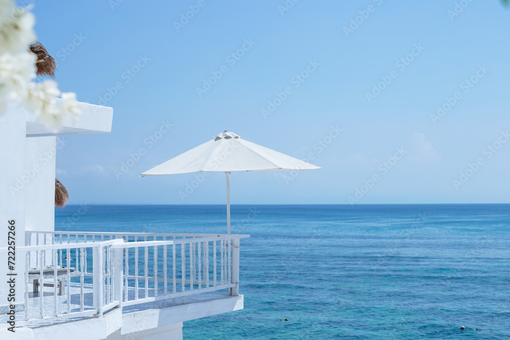 Fototapeta premium A large white umbrella on the balcony of the hotel with the ocean in the background. Leisure and travel concentrate with space for text