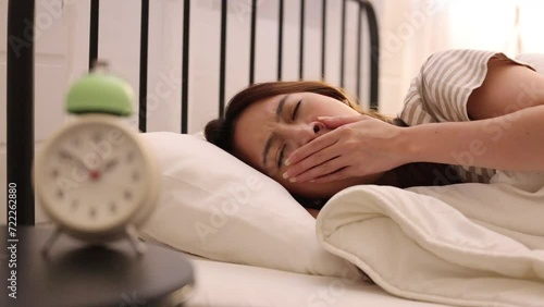 Asian woman yawn suffer from insomnia on her bed with a clock on bed side