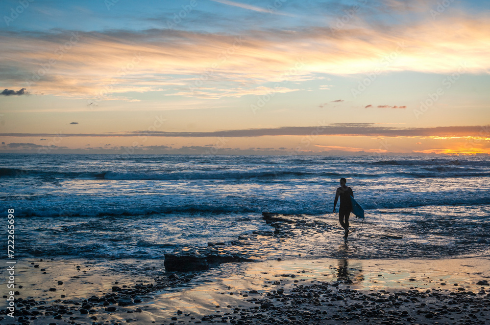 surfer walking on the beach at sunset