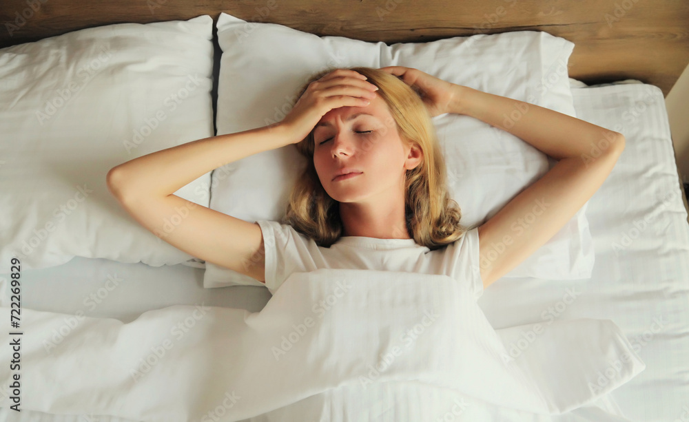 Woman with headache, pain tension in head, suffers from migraine lying in bed Woman with headache, pain tension in head, suffers from migraine lying in bed