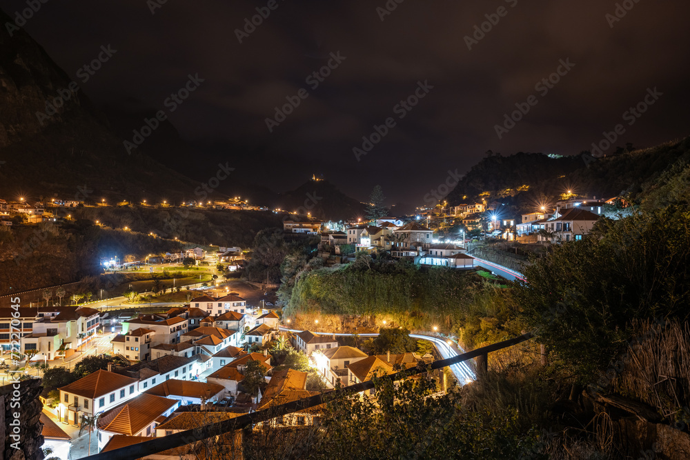Late night-time atmosphere, street lighting and car light trails of the picturesque village on the north coast in a green, overgrown valley. Sao Vincente, Madeira Island, Portugal, Europe.