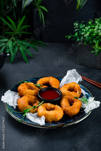 Crispy squid rings in dough with sauce and microgreens with chopsticks.