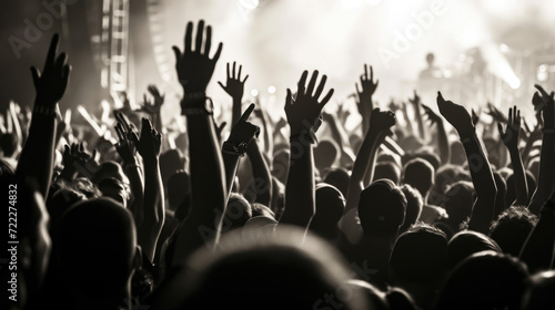 Monochrome image of a crowd at a concert, with many hands raised in the air, silhouetted against bright stage lights.