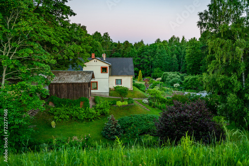 Nice backyard landscape with well kept lawn, flower beds, wooden barn and house at sunrise. Smiltene, Latvia.