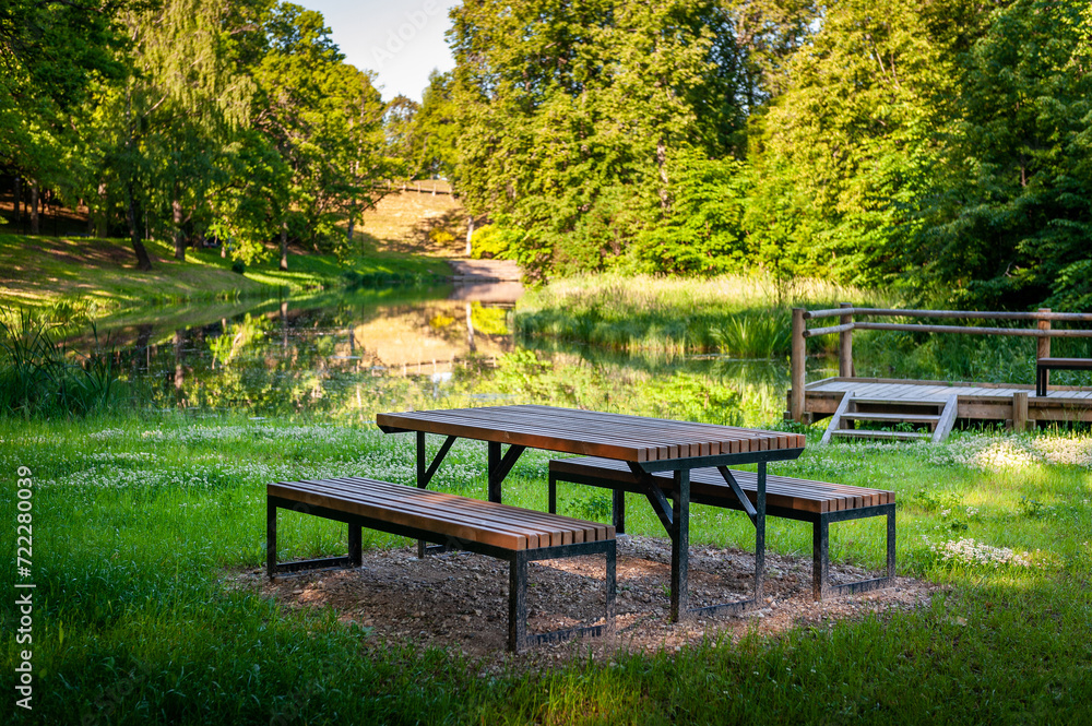 Wooden picnic tables near a river in Smiltene Old Park. Latvia. Recreational, picnic rest area in a park. Wooden picnic tables near a river in Smiltene Old Park. Latvia. Recreational, picnic rest area in a park.