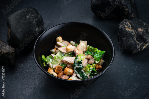 Fresh salad with chicken, lettuce, beans, croutons in bowl on a dark table.