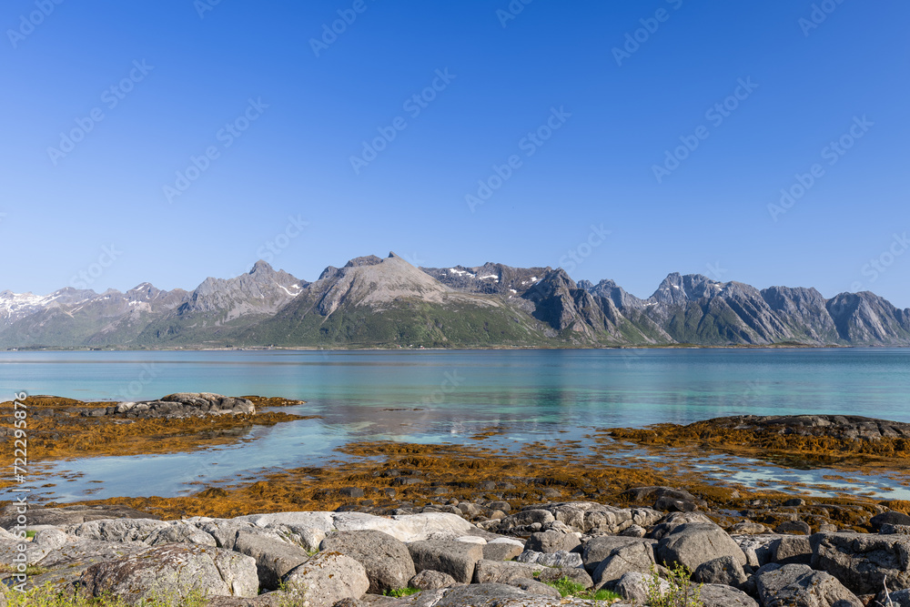 Serene beauty of the Lofoten Islands in Norway, showcasing the clear turquoise waters of the Norwegian Sea, contrasting with the rugged peaks of the mountains that rise dramatically in the background