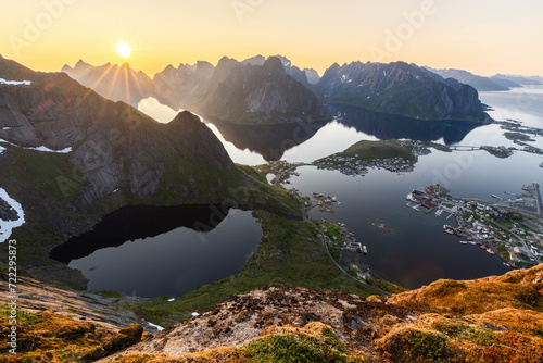 Golden hour glow blankets Reinebringen, Lofoten Islands, with the midnight sun cresting over sharp peaks, highlighting the village of Reine and reflective fjords