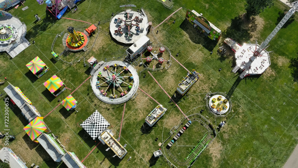 Aerial drone photo of a local carnival set in a green park setting. Rides shown are tilt a whirl, ferris wheel and many others.
