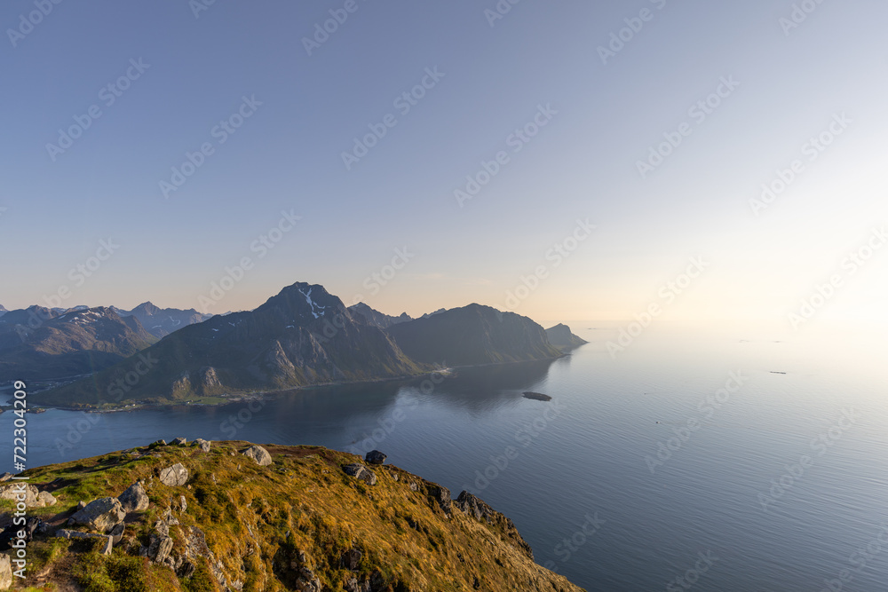 Soft light from the midnight sun bathes the rugged landscape of Offersoykammen, overlooking the tranquil Nappstraumen strait in the Lofoten archipelago