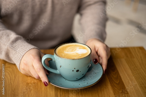 Womans Hands holding a cup of coffee over table. Still life with cup of latte. Coffee in ceramic blue cup on wooden table in cafe