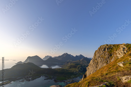 Soft sunlight of the midnight sun graces the peaks and cliffs near Nappstraumen in the Lofoten Islands, Norway, casting a gentle glow over the rugged landscape