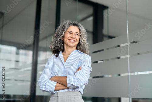 Happy mature business woman leader standing in office looking away. Smiling confident older middle aged professional lady corporate leader, senior female executive or entrepreneur portrait.