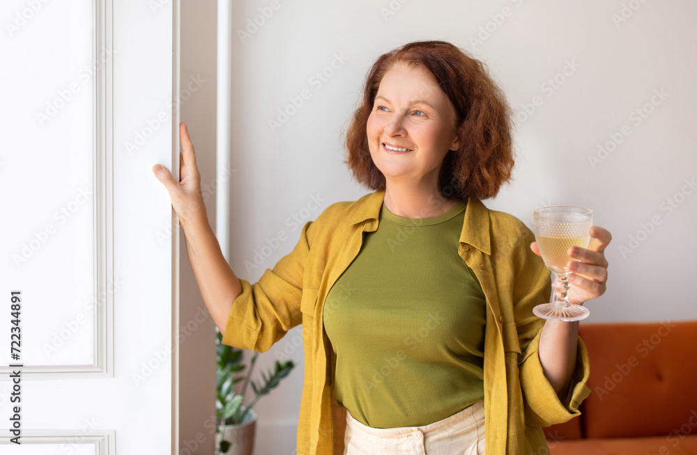 Relaxed senior woman holding glass of wine ad looking from window Relaxed senior woman holding glass of wine ad looking from window
