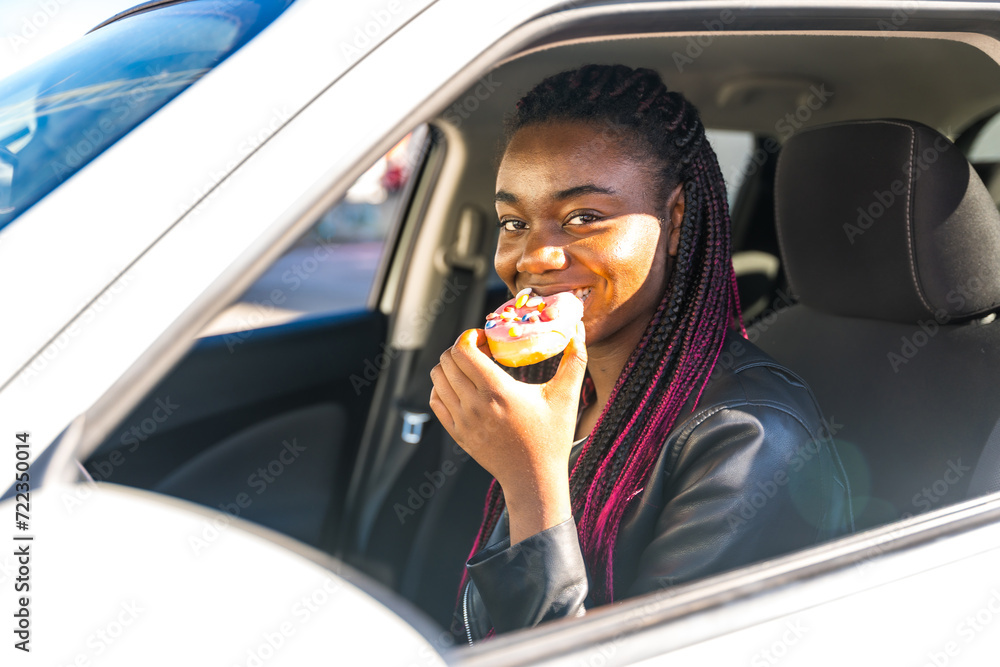Naklejka premium Cheerful african woman biting a doughnut sitting in a car